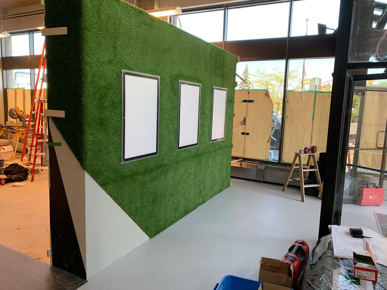 Panneau mural en gazon artificiel vert avec trois ouvertures rectangulaires à cadre blanc dans un espace atelier
