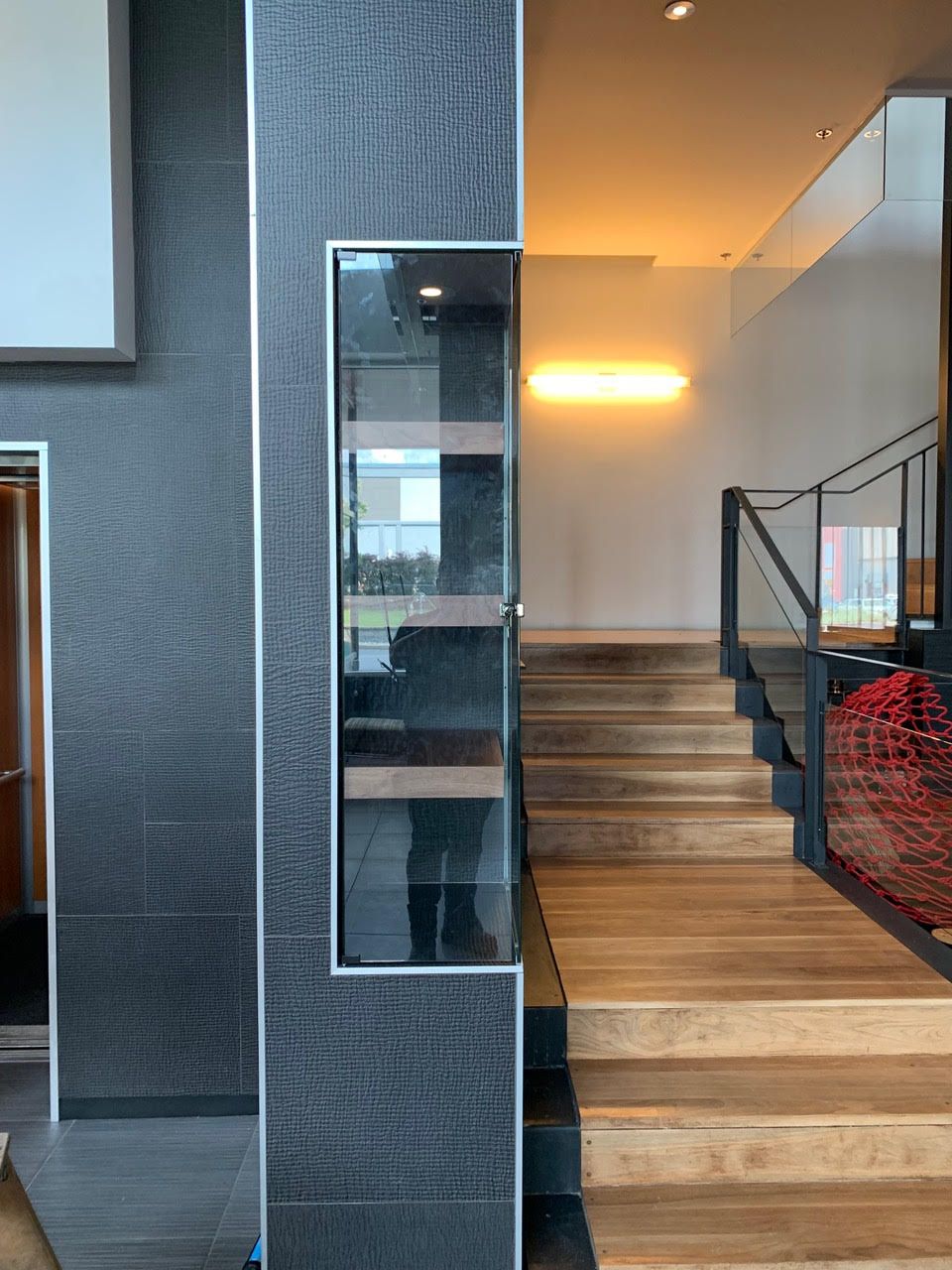 Escalier intérieur avec murs gris, marches en bois, rampe en verre et éclairage mural chaleureux
