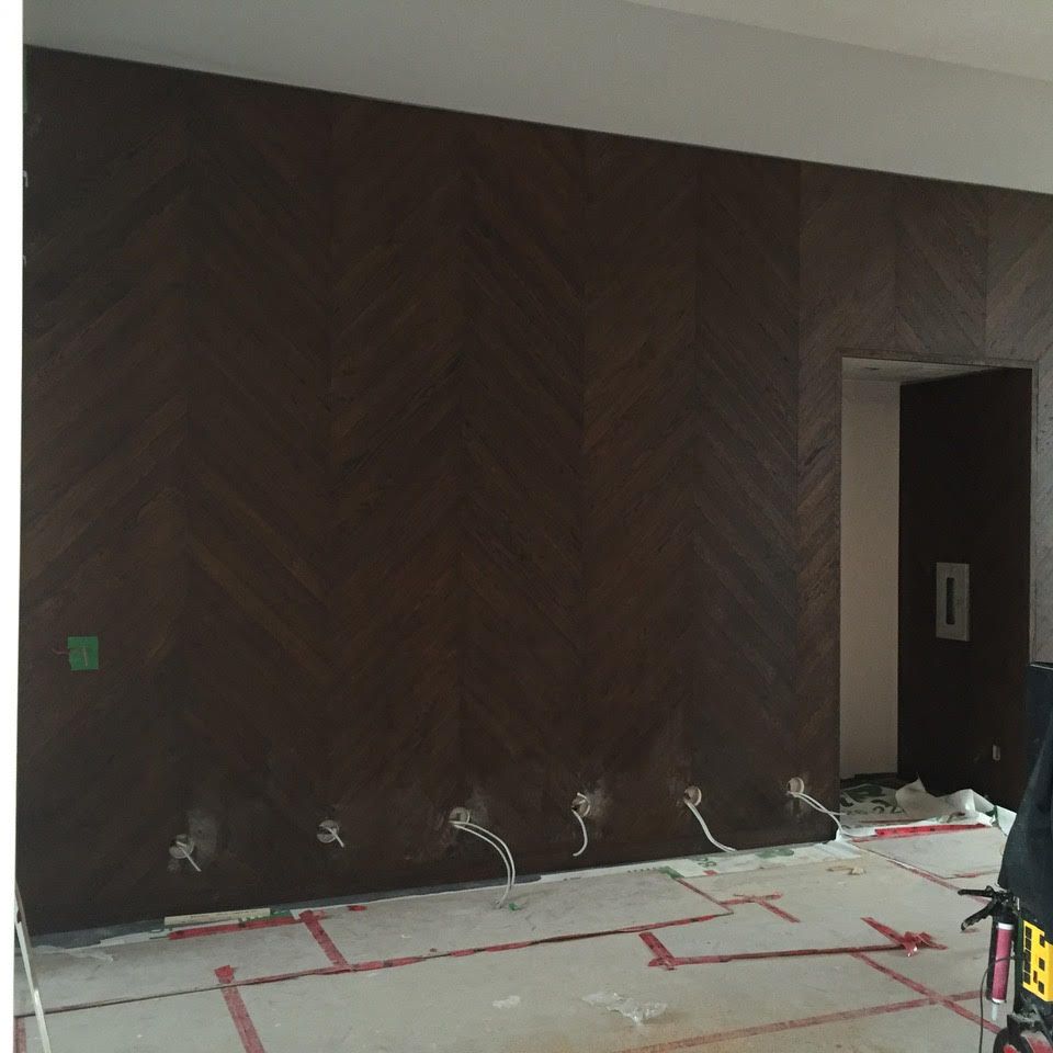 Mur intérieur en rénovation avec panneaux de bois foncé, tuyaux apparents et sol recouvert près d'une porte ouverte