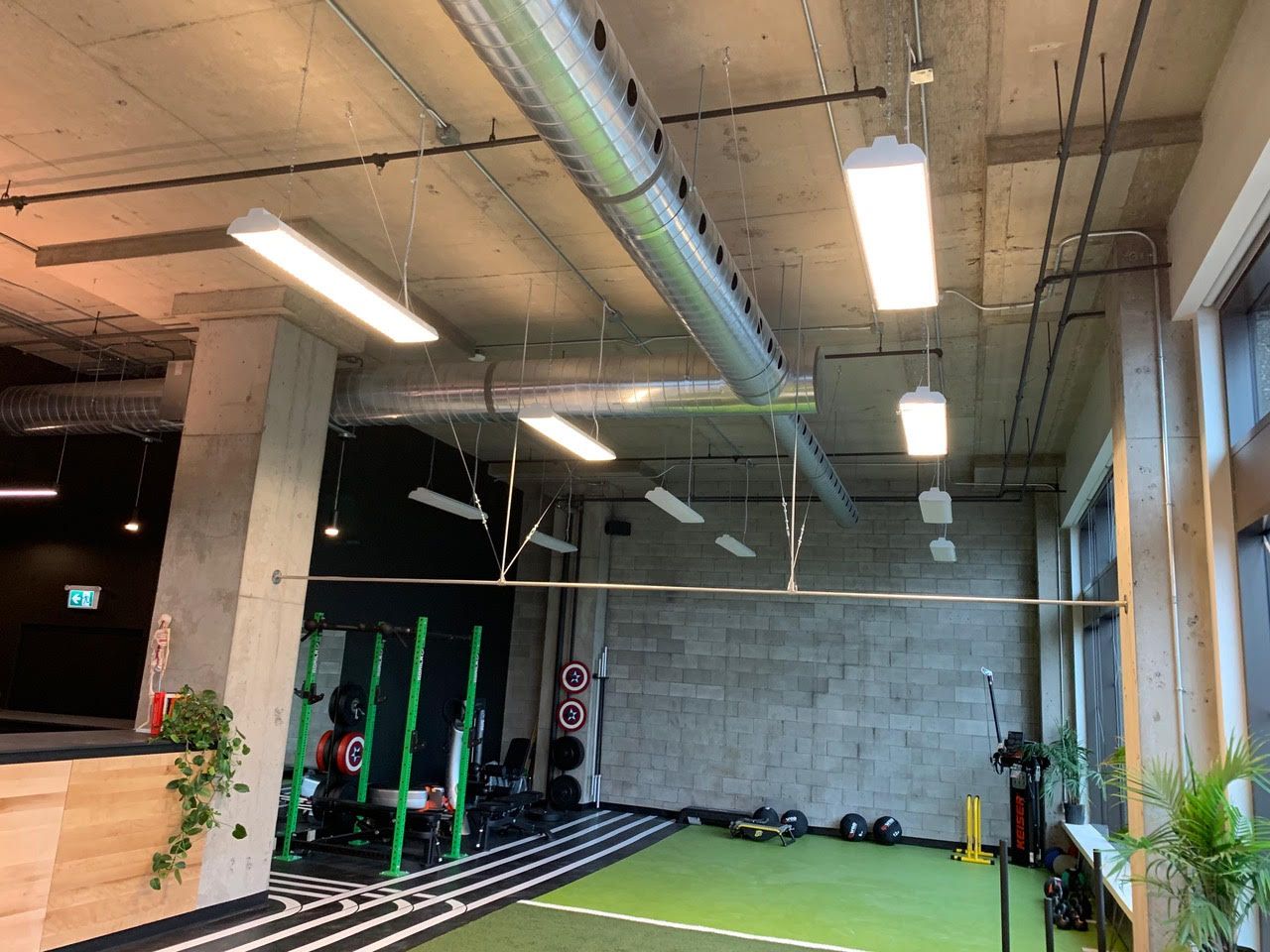Intérieur de salle de sport de style industriel avec piliers en béton, supports de musculation, tapis et luminaires suspendus