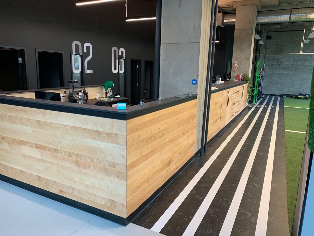 Bureau d'accueil moderne avec panneaux de bois, comptoir noir et sol à rayures dans un intérieur lumineux