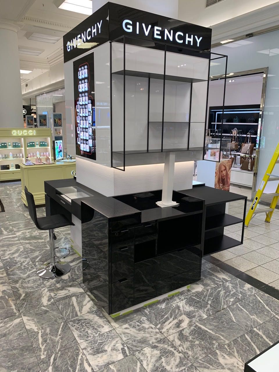 Kiosque d'exposition Givenchy vide dans un centre commercial, noir et gris avec logo de la marque en hauteur.