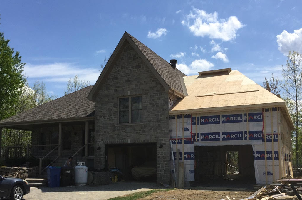 Maison en pierre avec une extension de toit partiellement construite sous un ciel bleu, entourée de matériaux de construction.