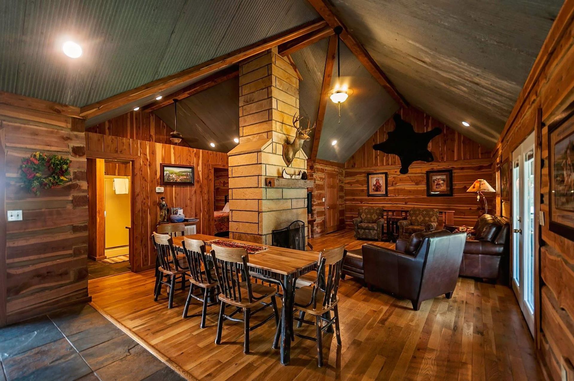 Rustic cabin interior with wooden walls, bar, fireplace, and leather furniture.