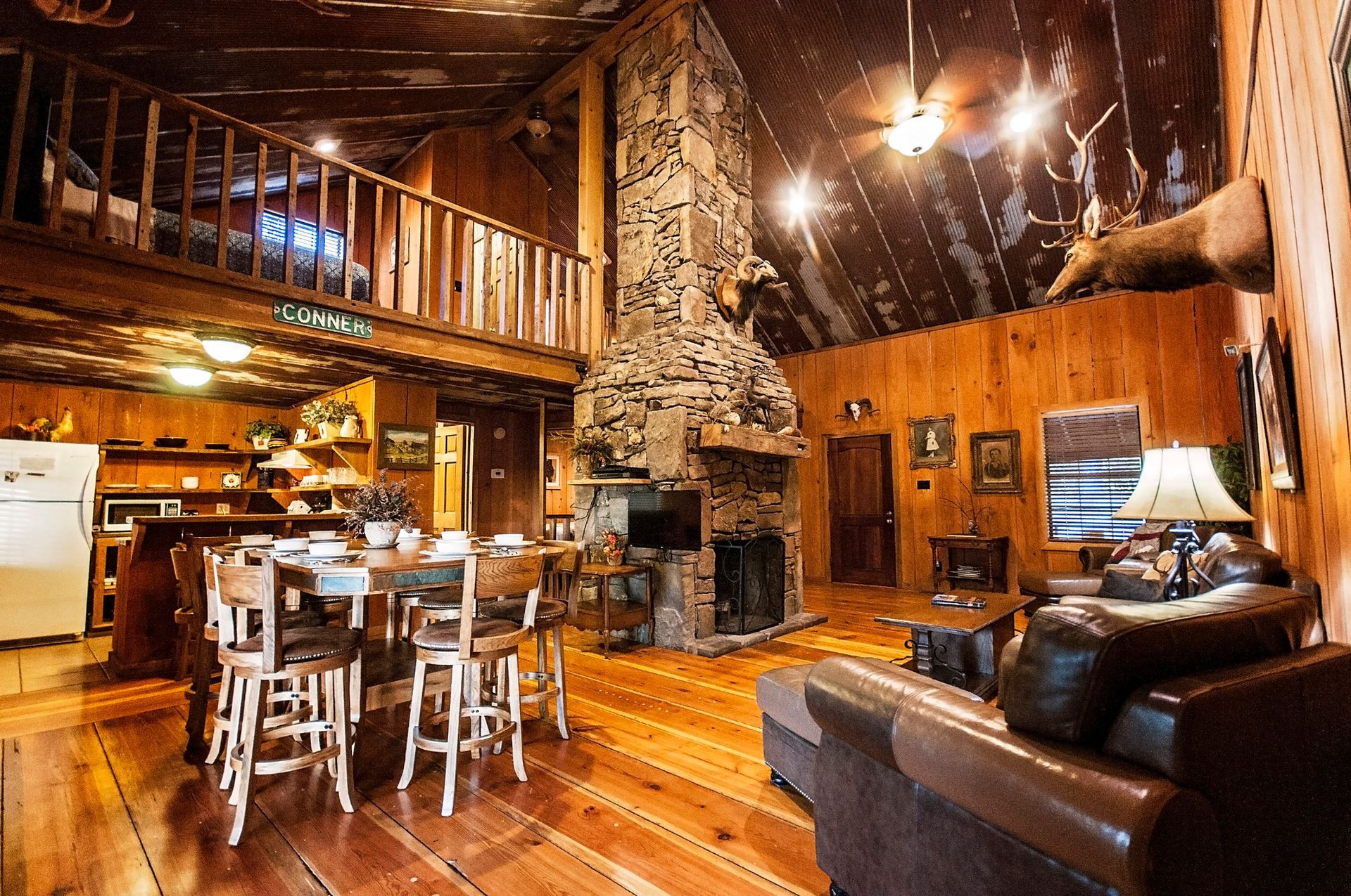 Rustic cabin interior with fireplace, loft, and wooden furniture.