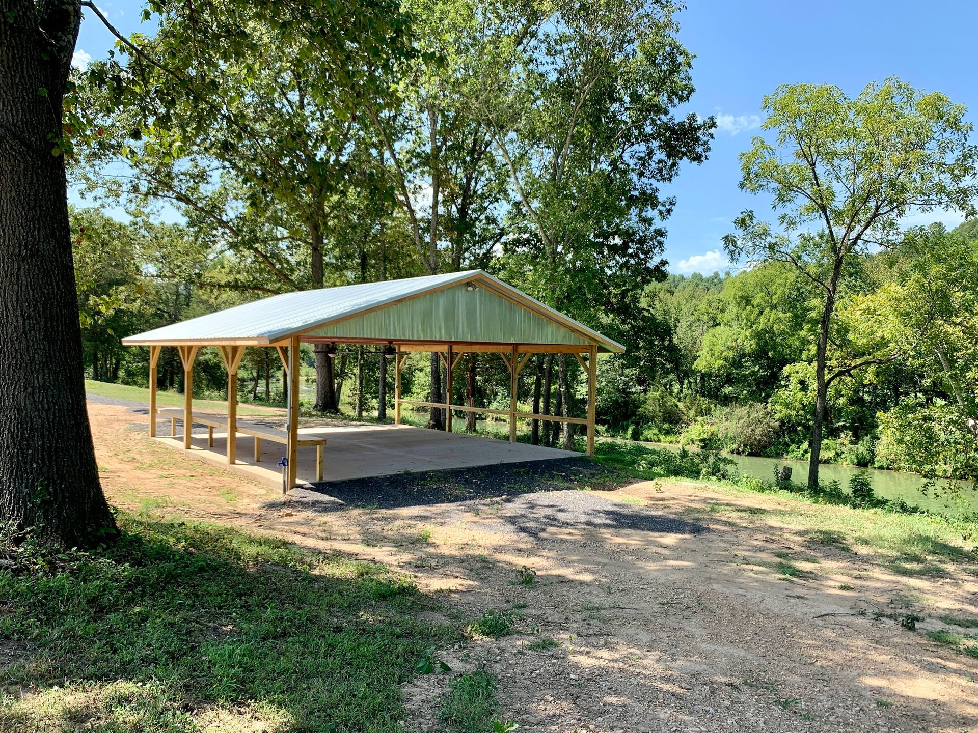 Wooden pavilion with metal roof in a park, surrounded by trees.