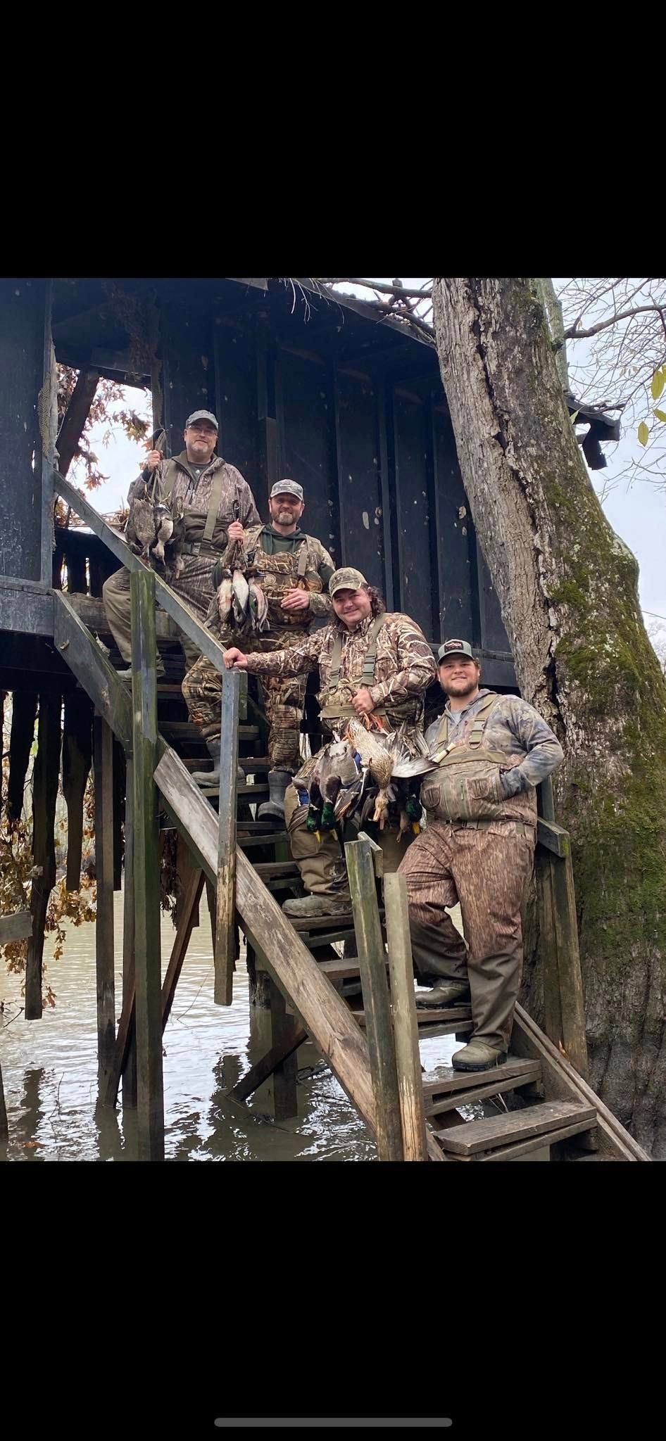 Soldiers in camouflage descending a wooden staircase beside a tree in an outdoor wooded area