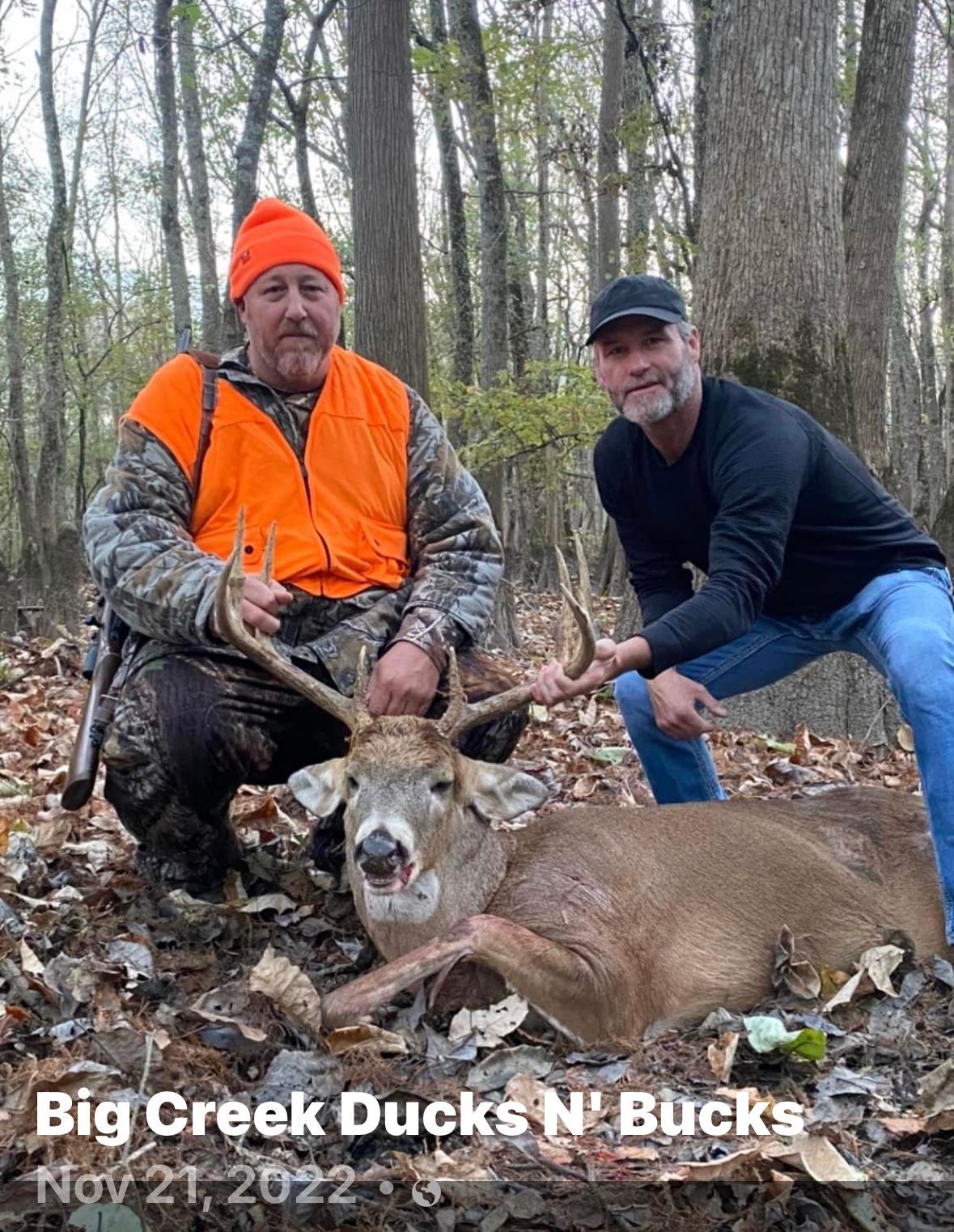 Two men posing with a deer in a wooded area, one in orange hunting gear, with “Big Creek Ducks N’ Bucks” text.