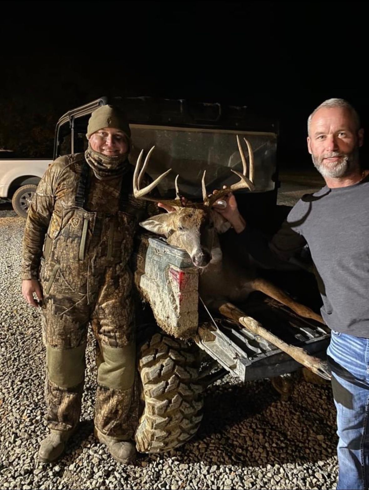 Two men posing with a large buck deer on a truck tailgate at night