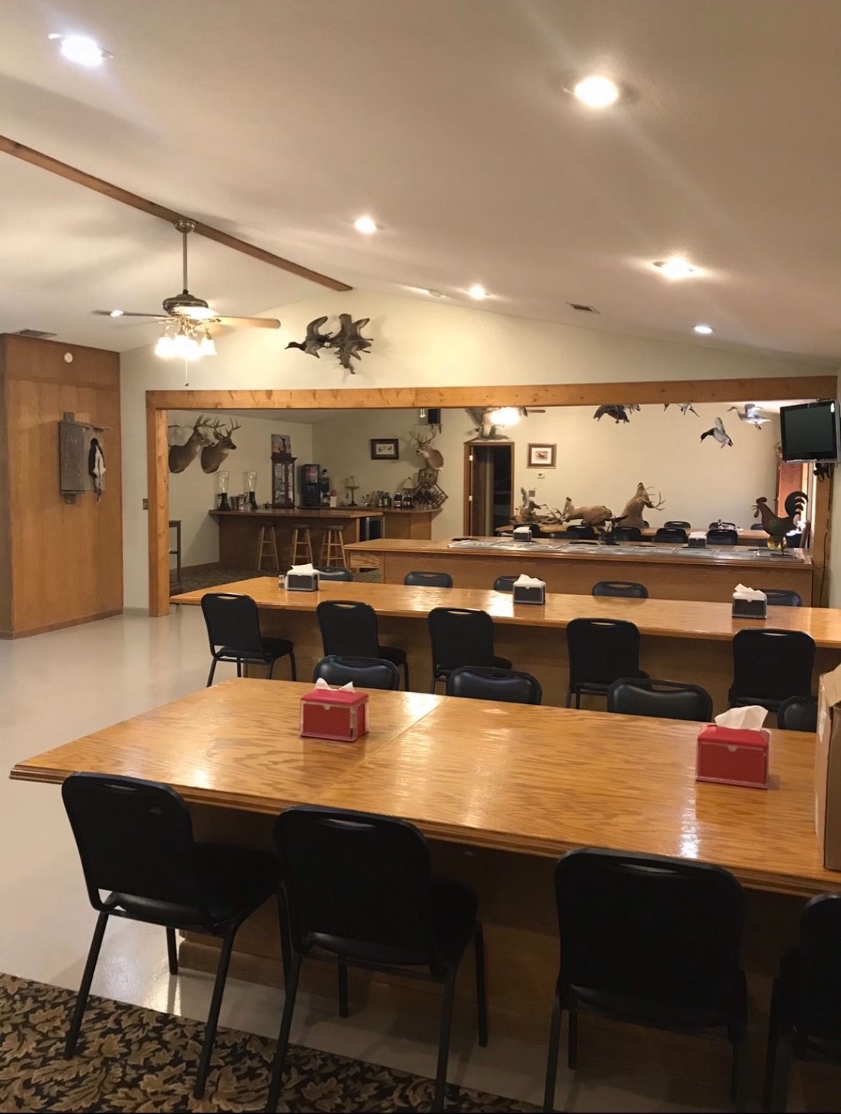 Empty meeting room with long wooden tables, black chairs, wall mirror, and ceiling lights