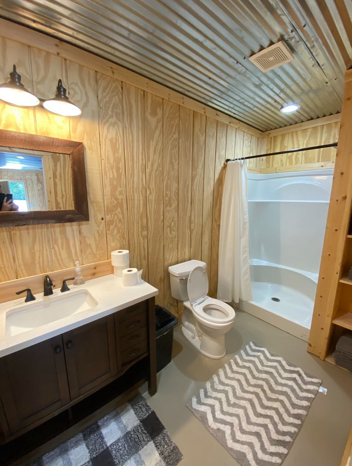 Cozy wood-paneled bathroom with vanity, toilet, shower-tub, and patterned rugs