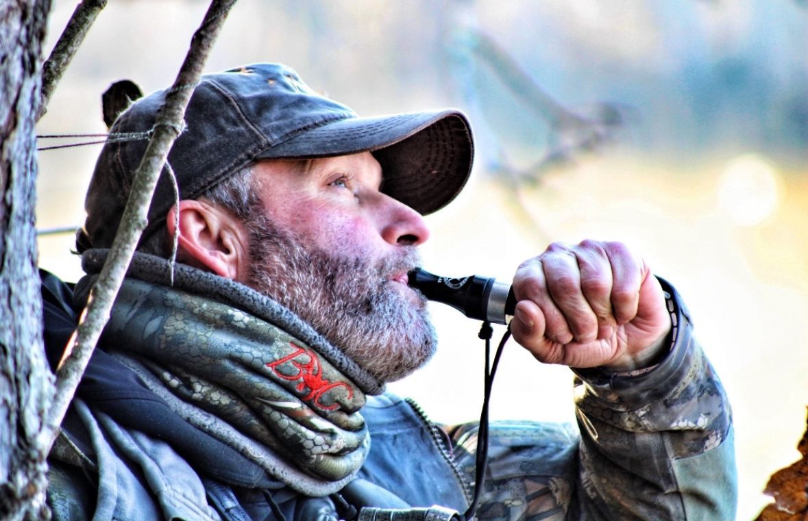 Camouflaged hunter blowing a call in a wooded outdoor setting