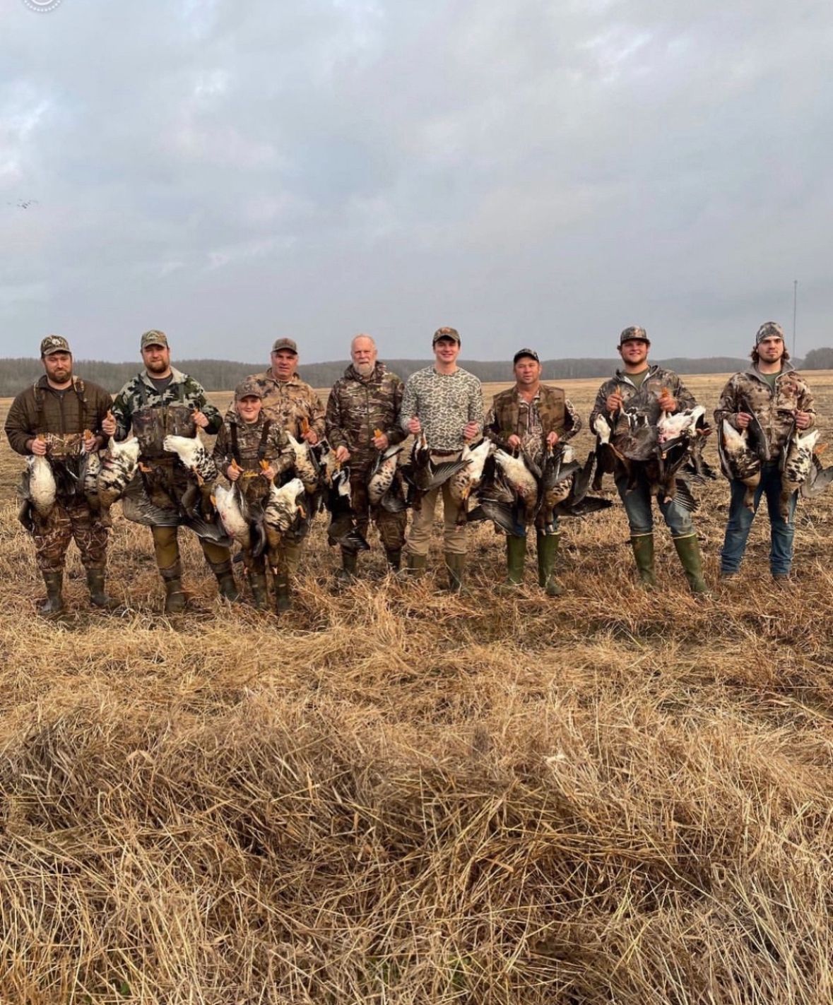 Hunters posing in a field with several retrieved birds on a cloudy day