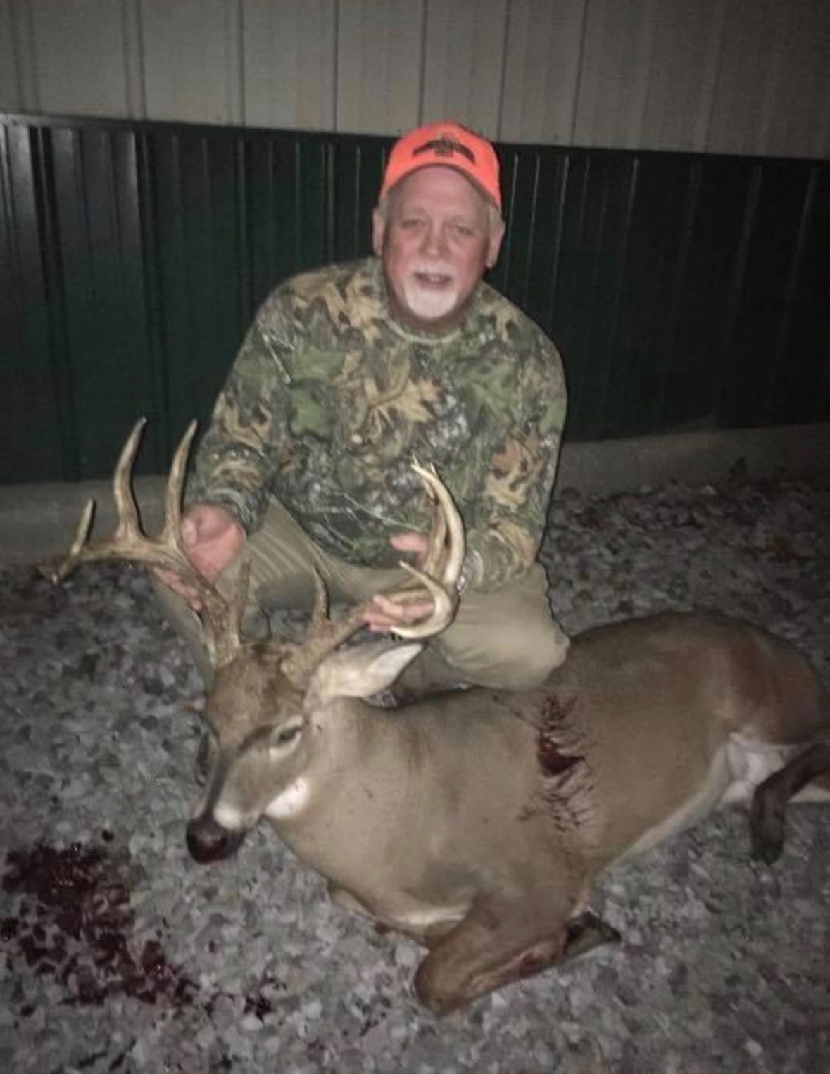 Hunter kneeling beside a large deer at night, wearing camouflage and an orange cap