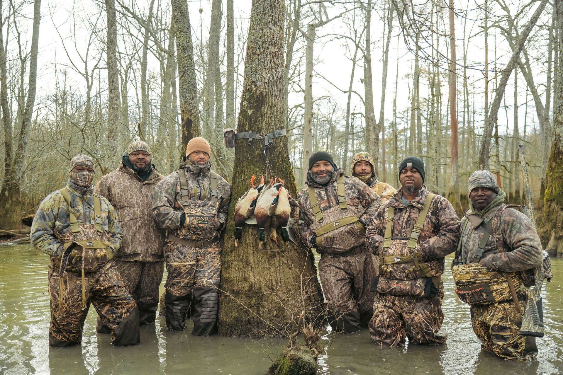 Camouflaged hunters posing with a deer in a flooded woodland with bare trees
