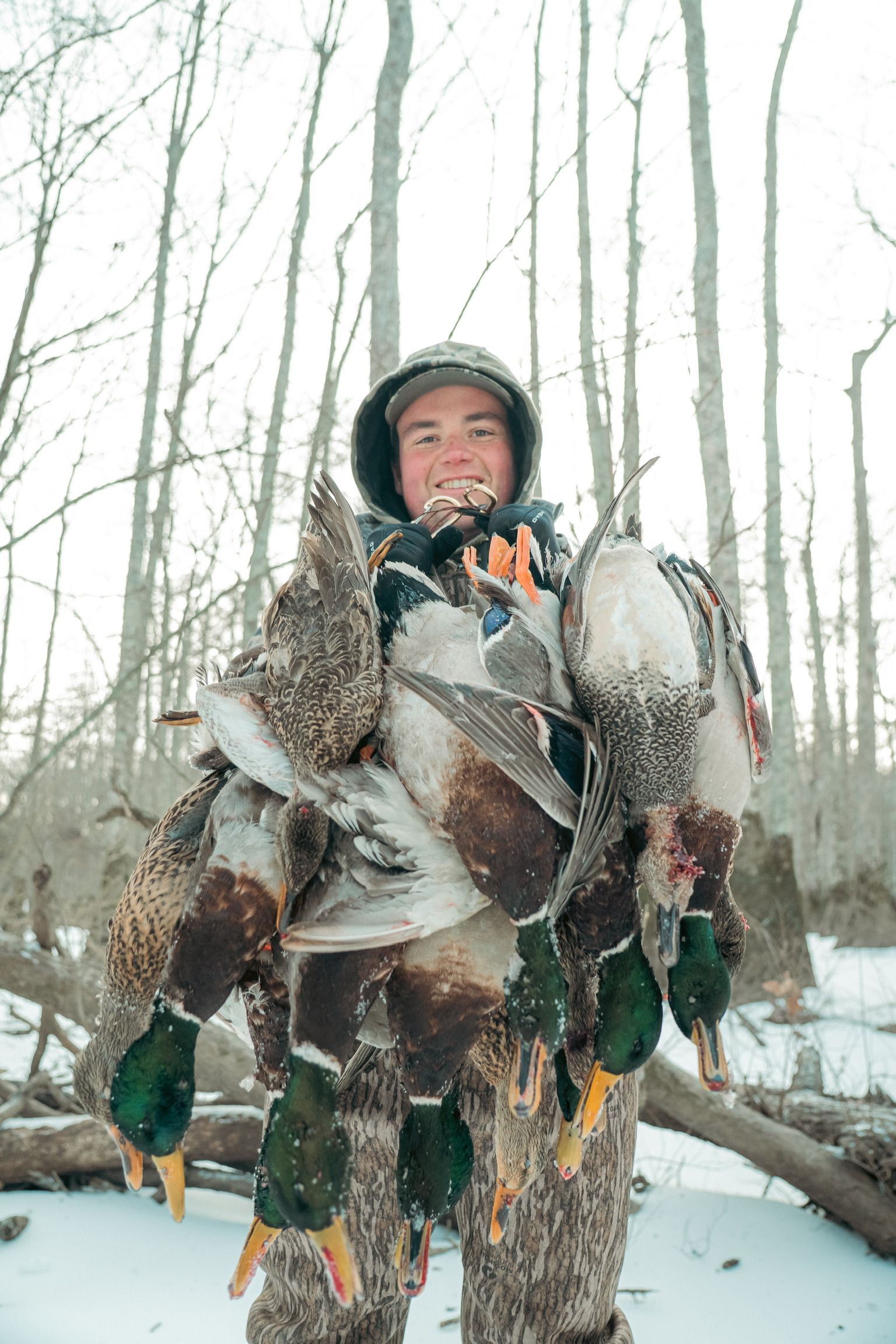 Hunter in winter gear holding several ducks in a snowy forest
