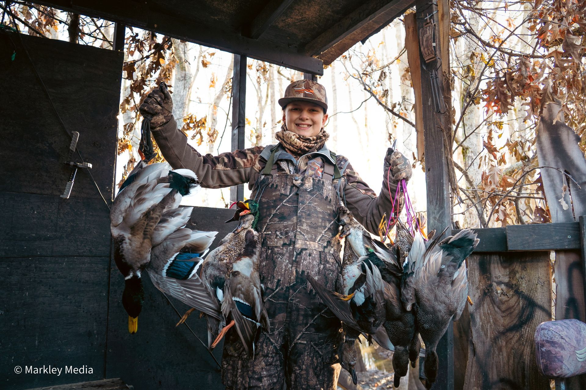 Hunter posing with a dead deer in a camouflaged deer stand in the woods