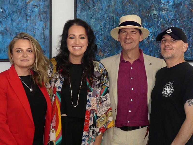 Anthony Carey with visitors standing in front of abstract paintings at an exhibition opening