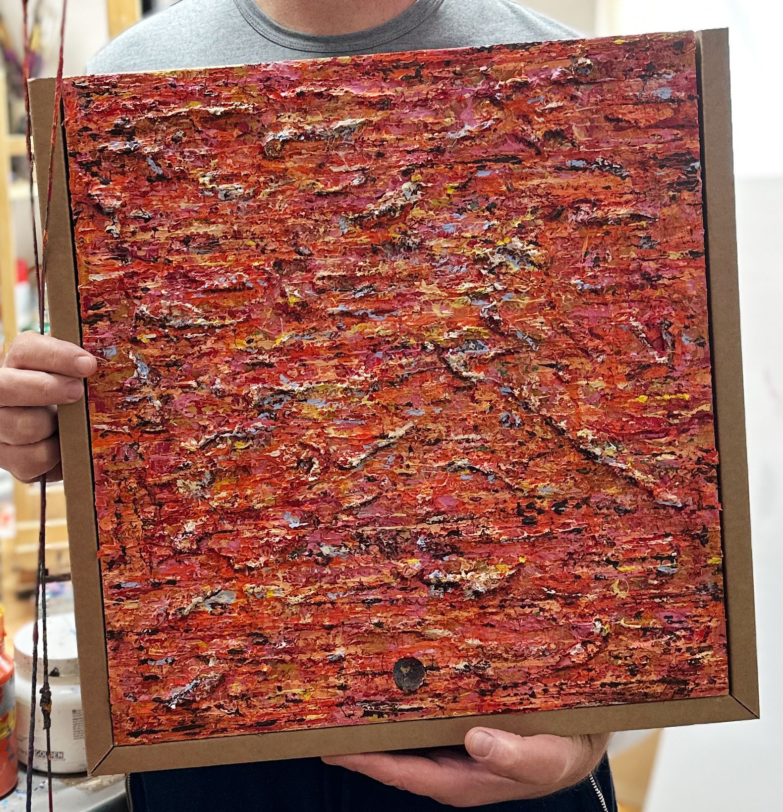 The artist holds a Heavily `Textured art on a pizza box 
