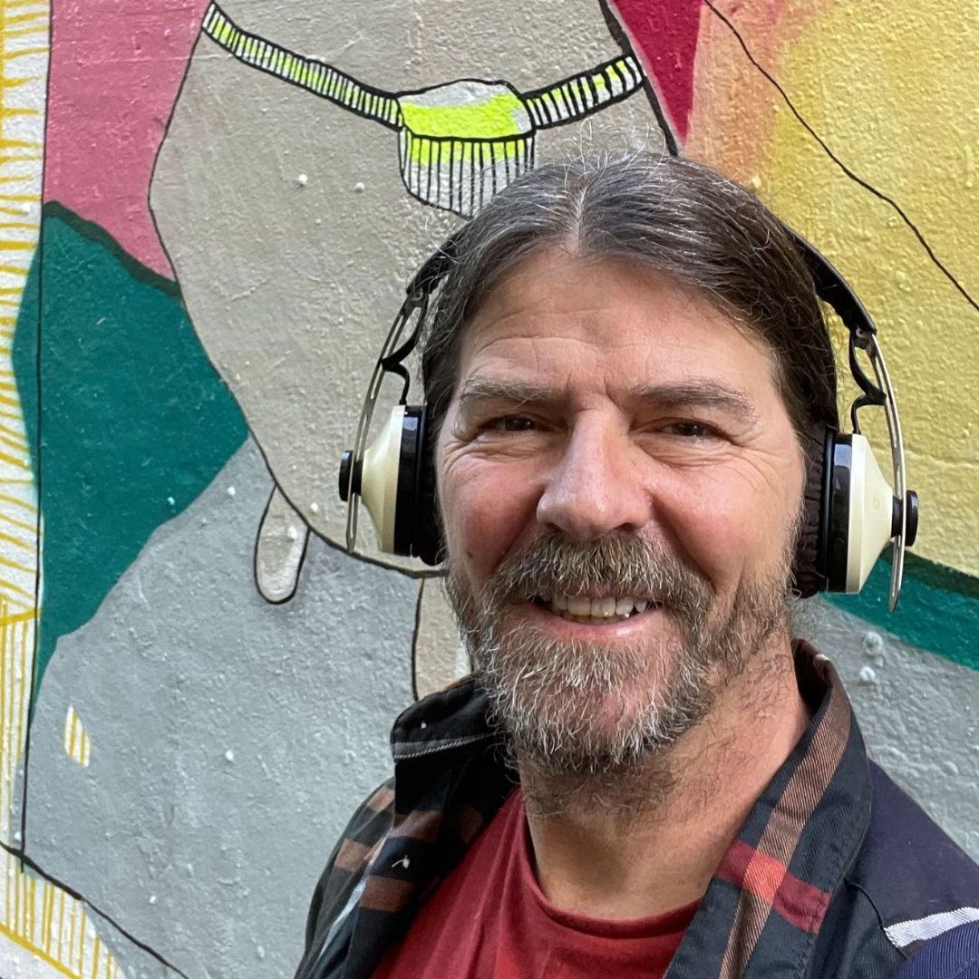 Head shot of the artist, Anthony Carey wearing headphones in front of mural in Dublin