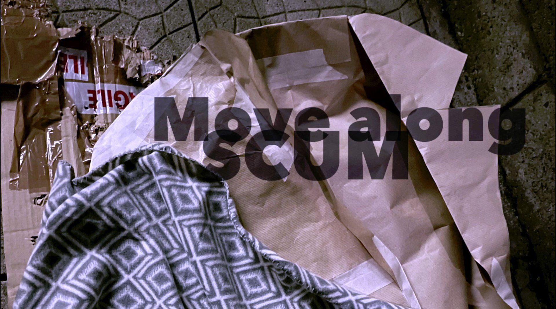 Still from Story showing cardboard on pavement, a patterned blanket, and a paper coat, with the words “Move along SCUM” overlaid