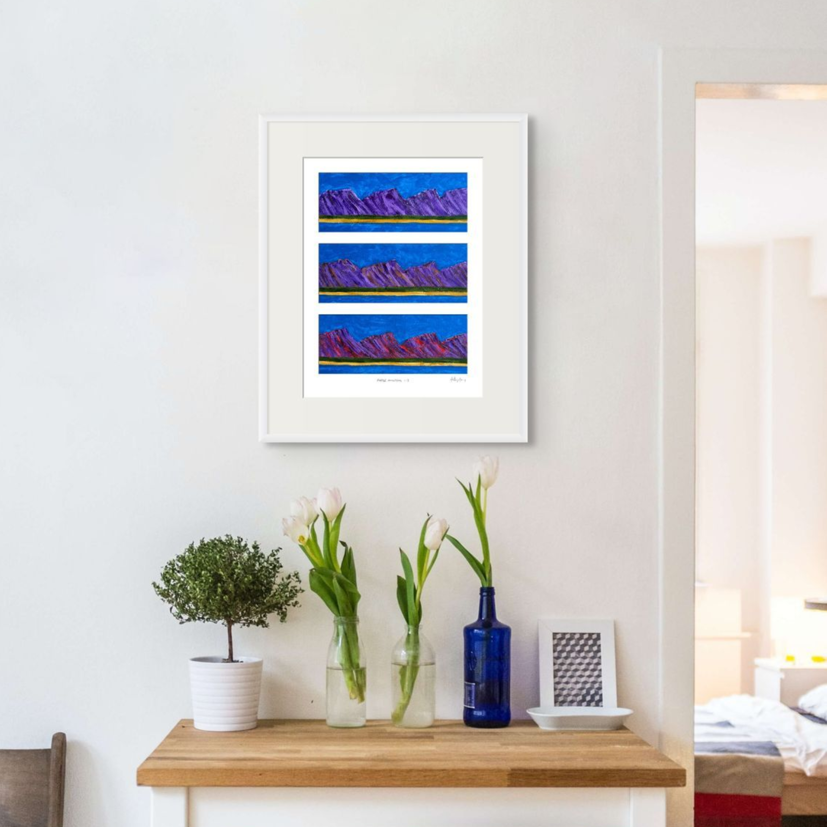Framed Anthony Carey artwork hanging above a wooden console table, showing how a smaller painting can suit an intimate interior space
