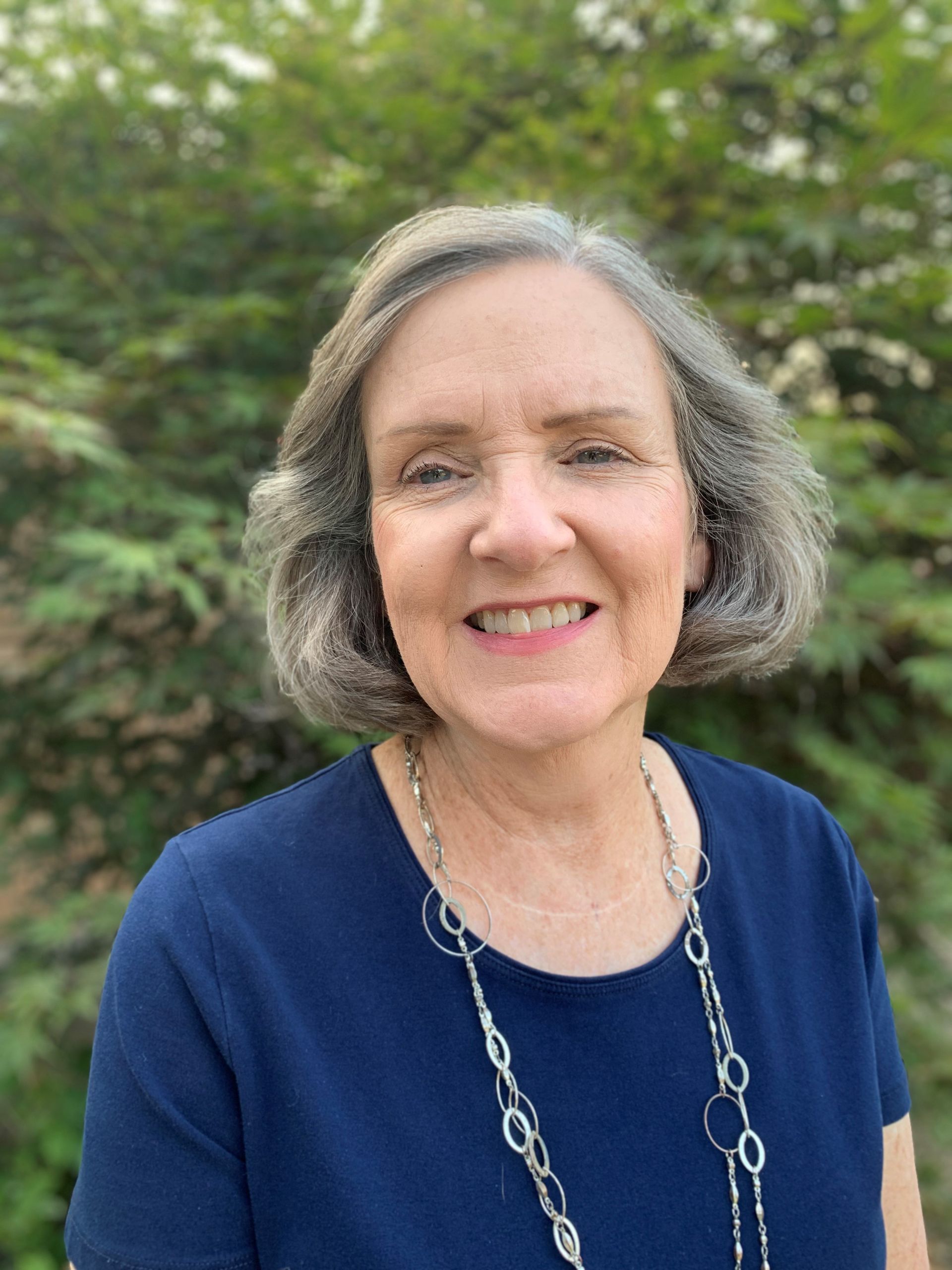 A woman in a blue shirt and necklace is smiling for the camera.