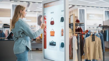 Vrouw die in een kledingwinkel een touchscreen gebruikt om handtassen te bekijken.