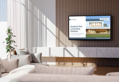 Woonkamer met tv waarop een advertentie voor luxe onroerend goed wordt getoond. Houten lambrisering, witte bank en natuurlijk licht.