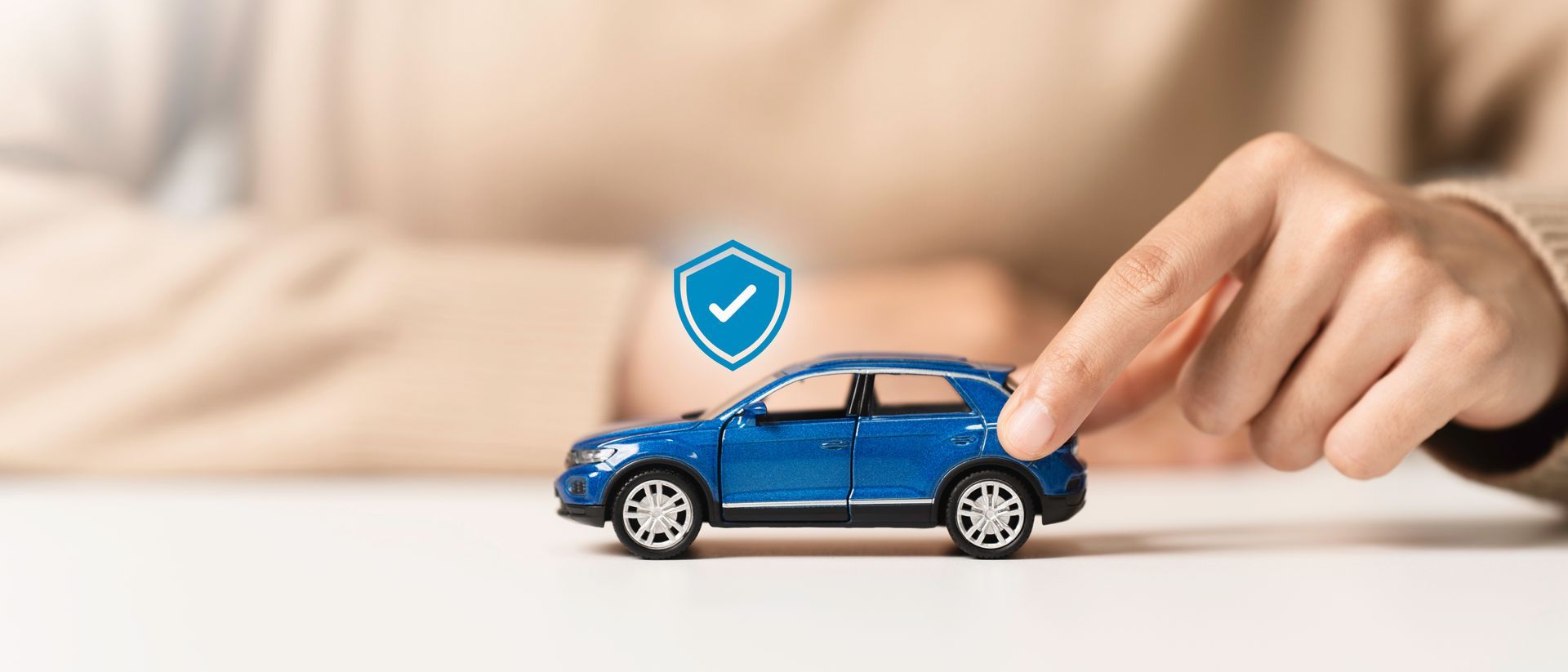 Blue toy car with shield icon, held by a hand on a table