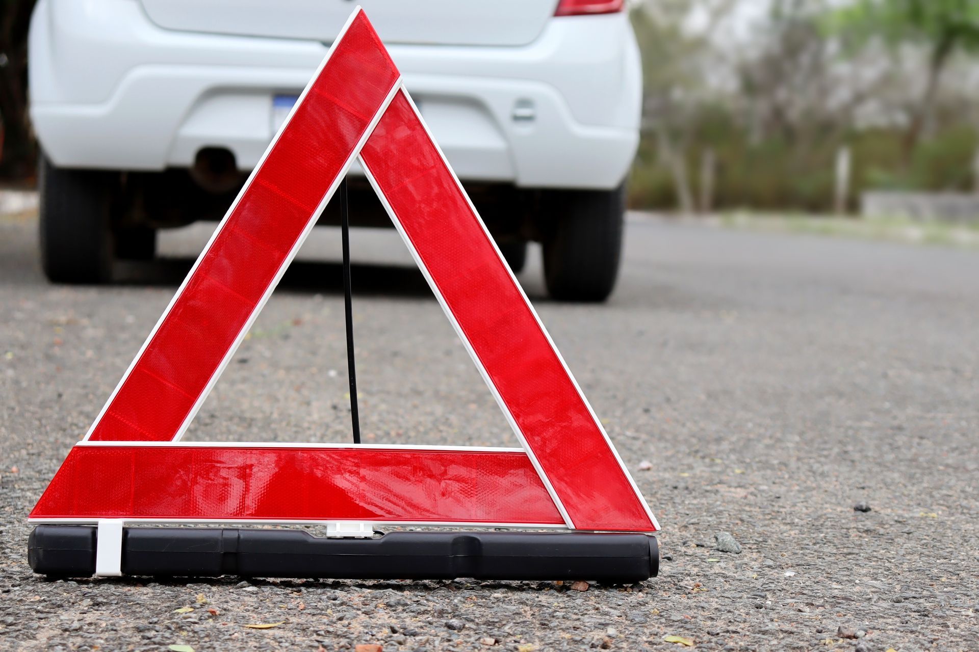 Red warning triangle on roadside in front of a white car.