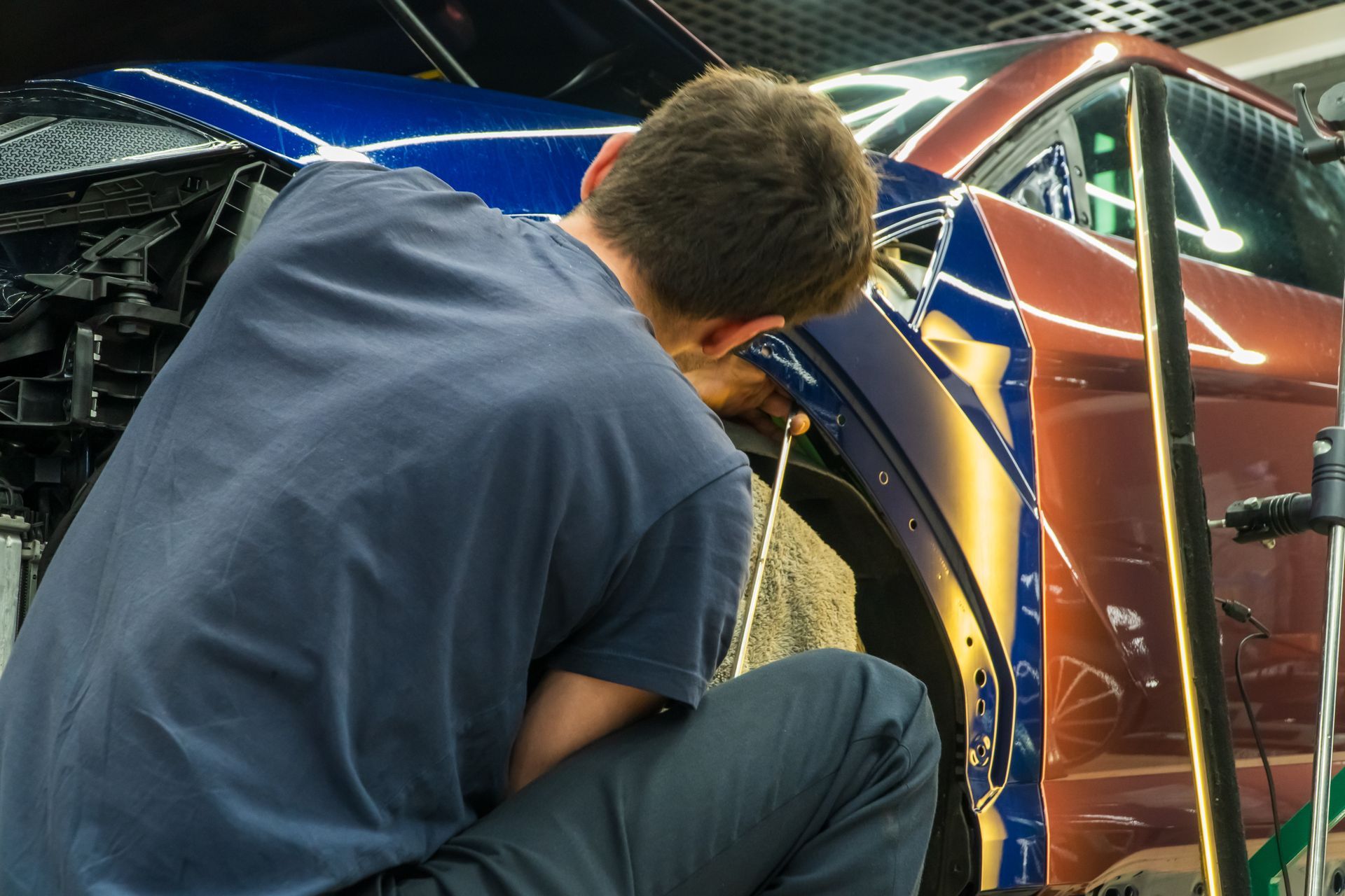 Worker inspecting a blue car’s body panel with tools in an auto repair shop
