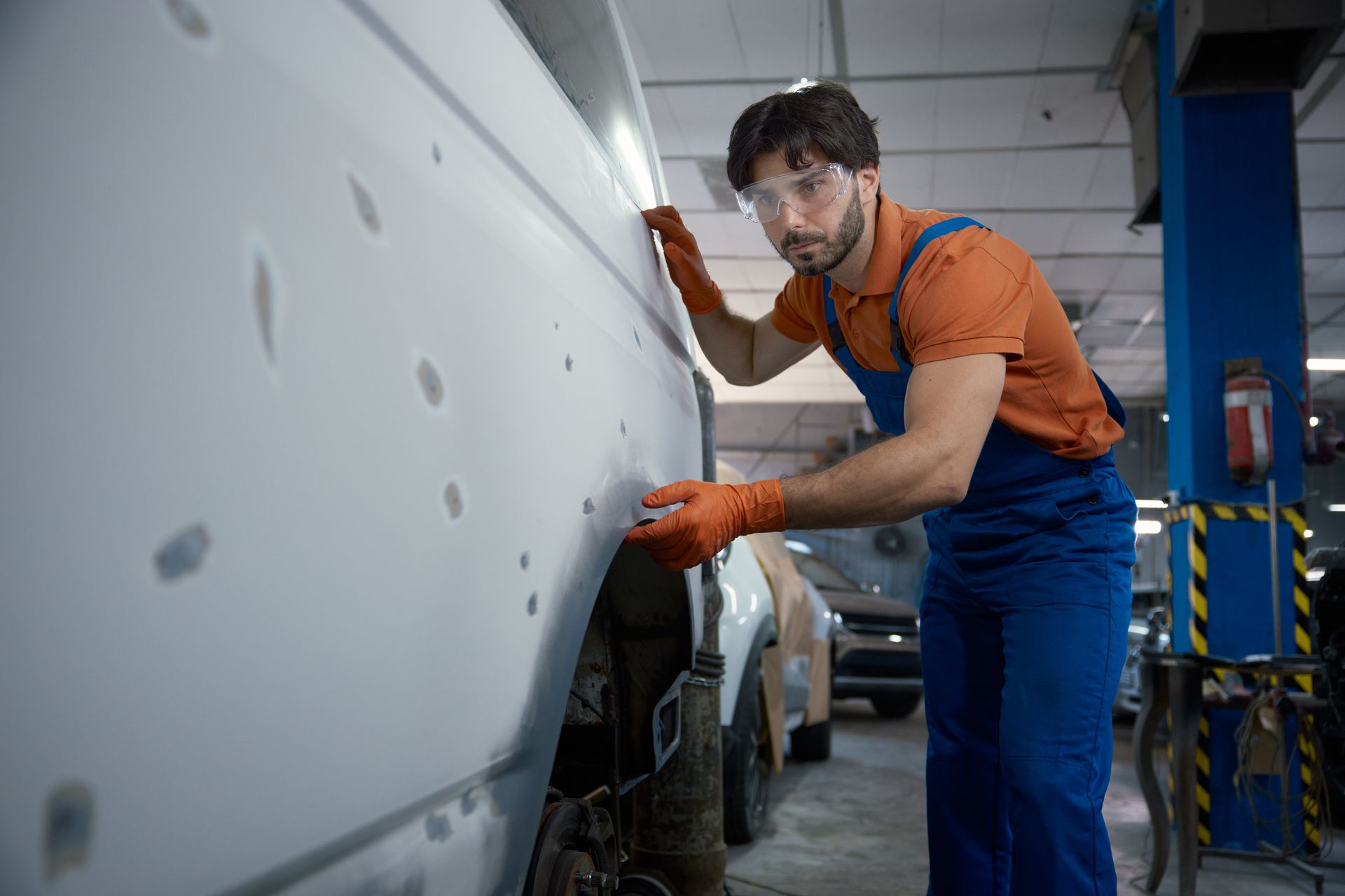 Mechanic in orange overalls polishing a white car in an auto repair shop