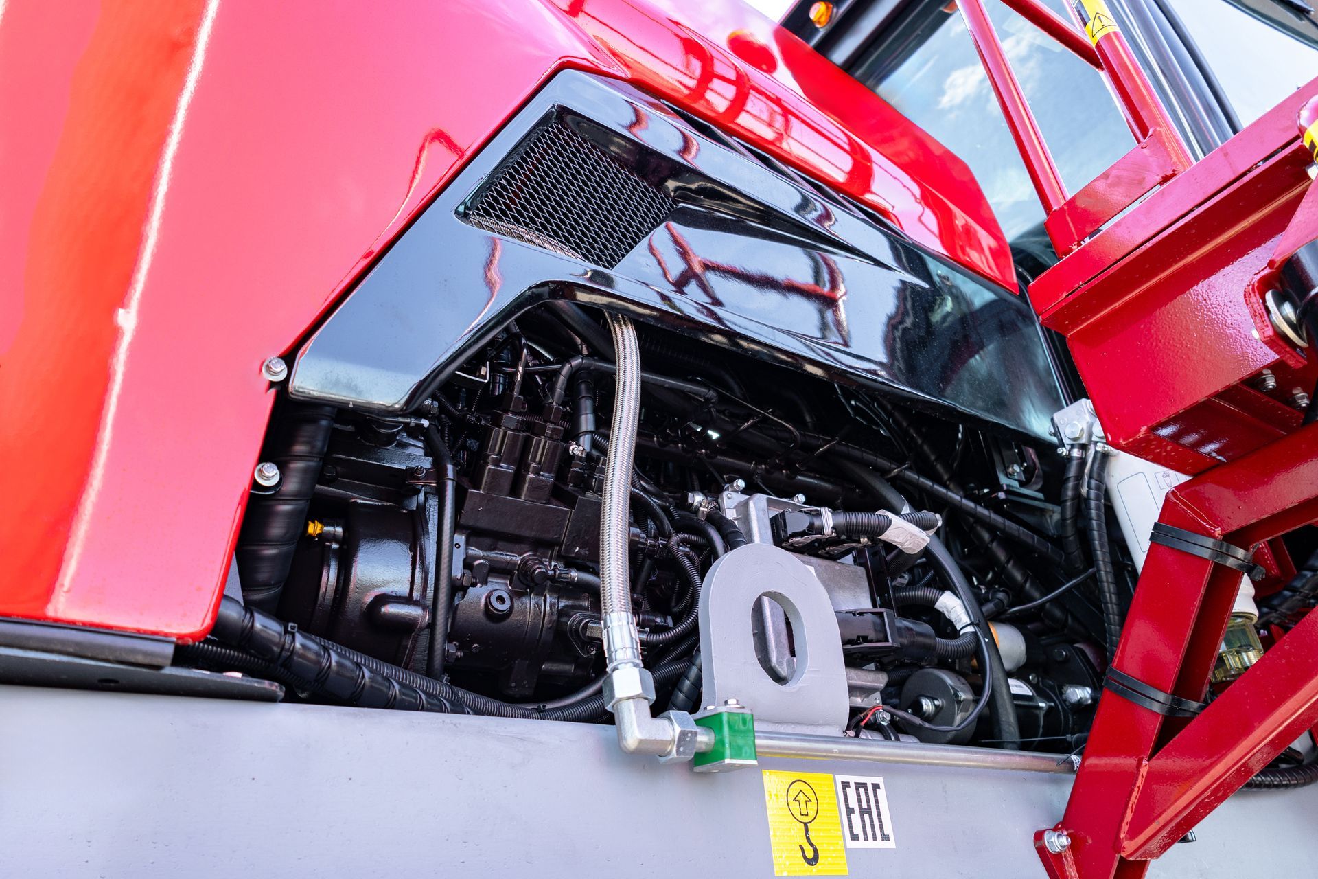 Close-up of a red vehicle engine compartment with exposed black machinery and hoses.