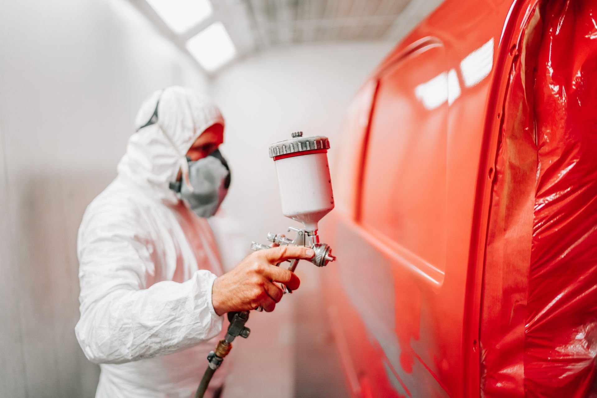 Worker in white protective suit spray-painting a red object in a workshop
