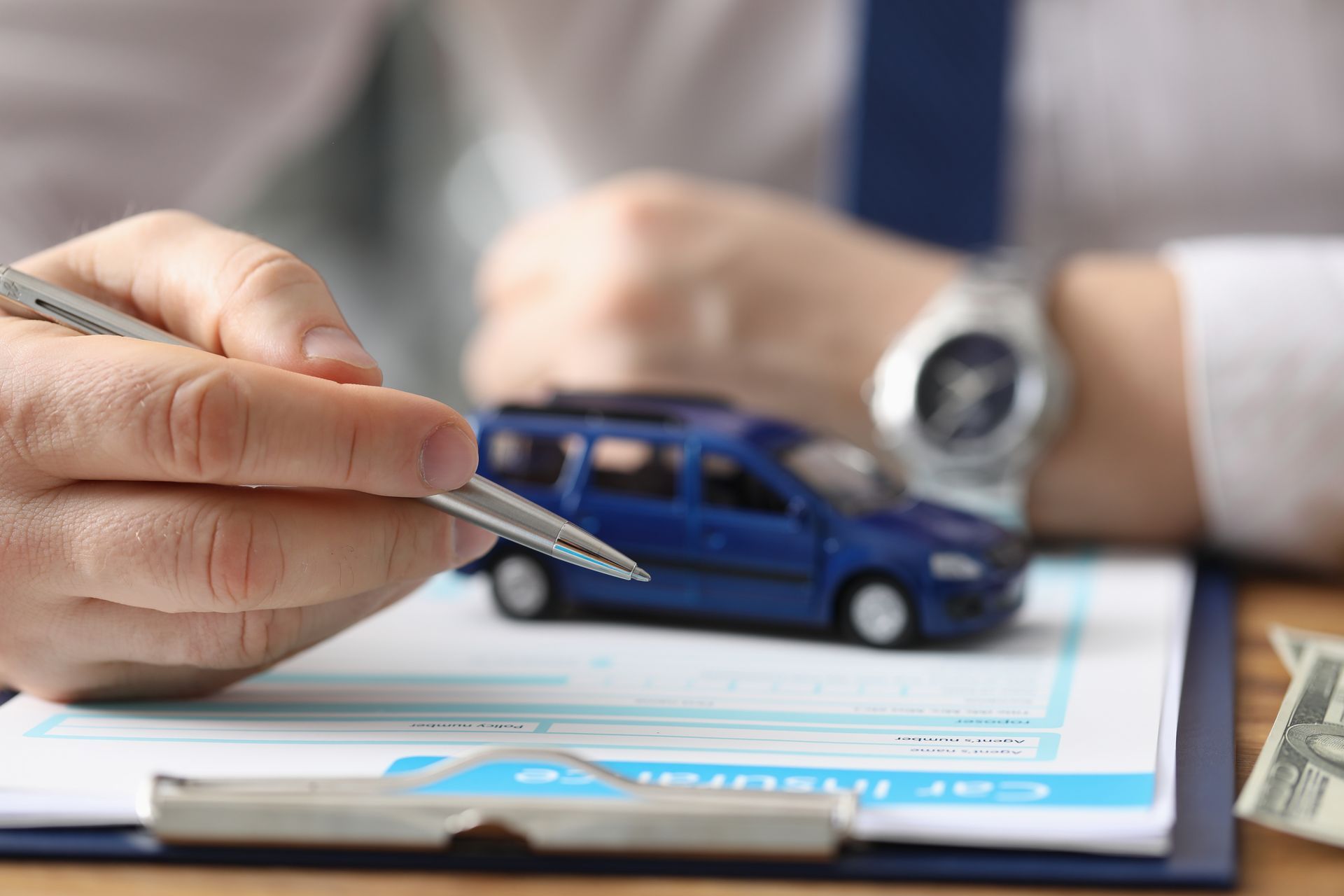 Hand placing a toy blue car on a clipboard during an insurance claim review