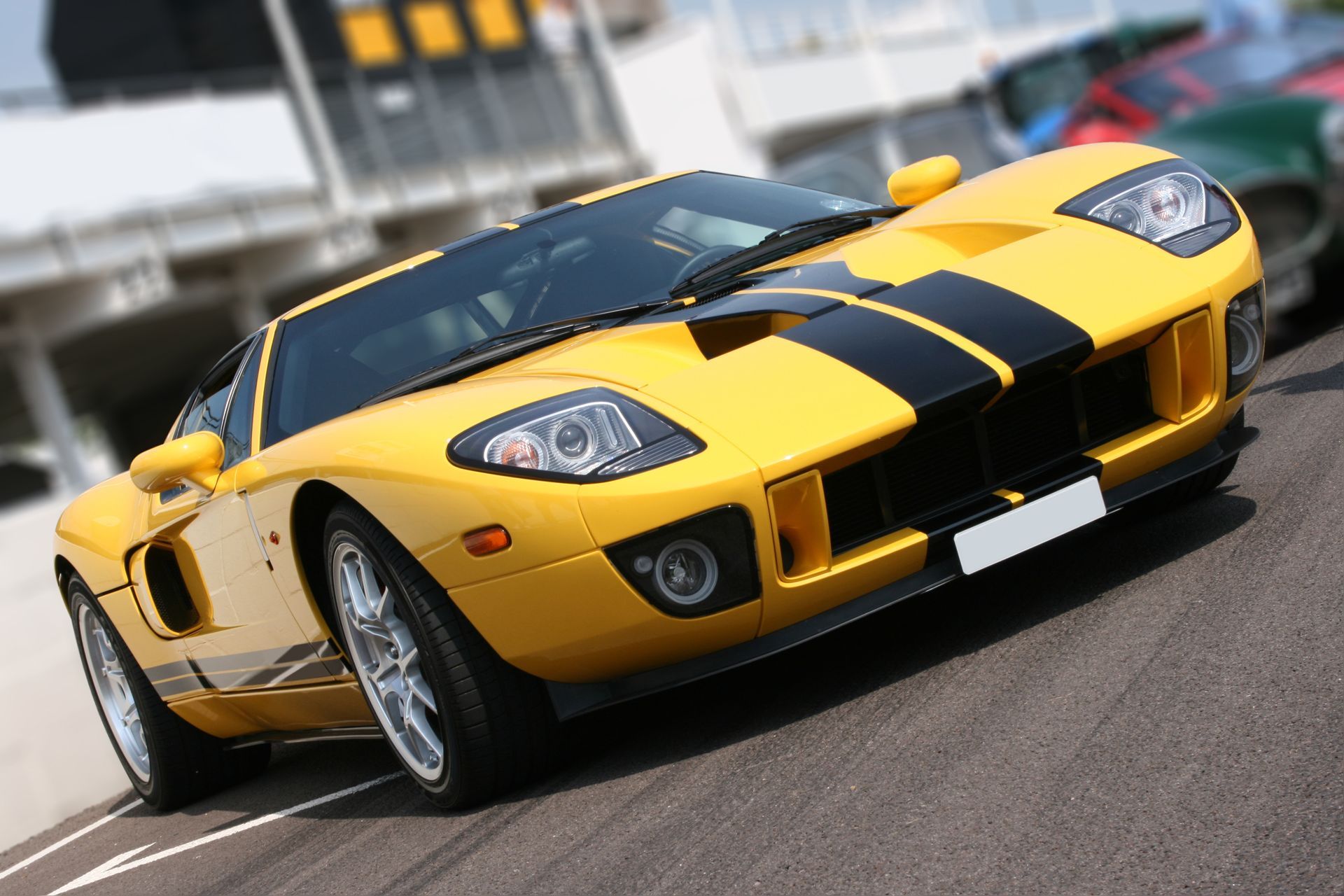 Yellow sports car with black racing stripes on a track, angled toward the camera