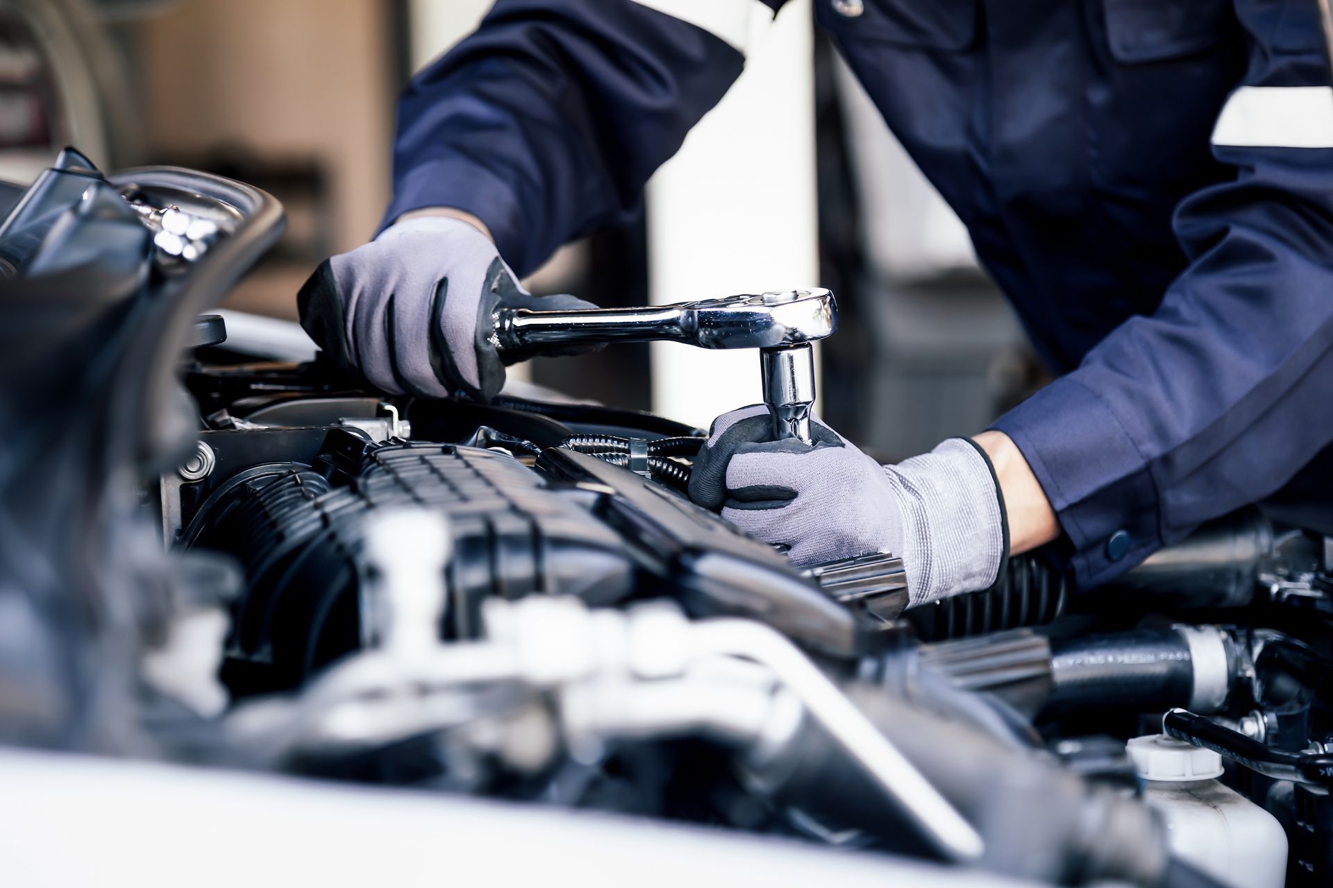 Mechanic in gloves inspecting an engine bay with a wrench in a car repair shop