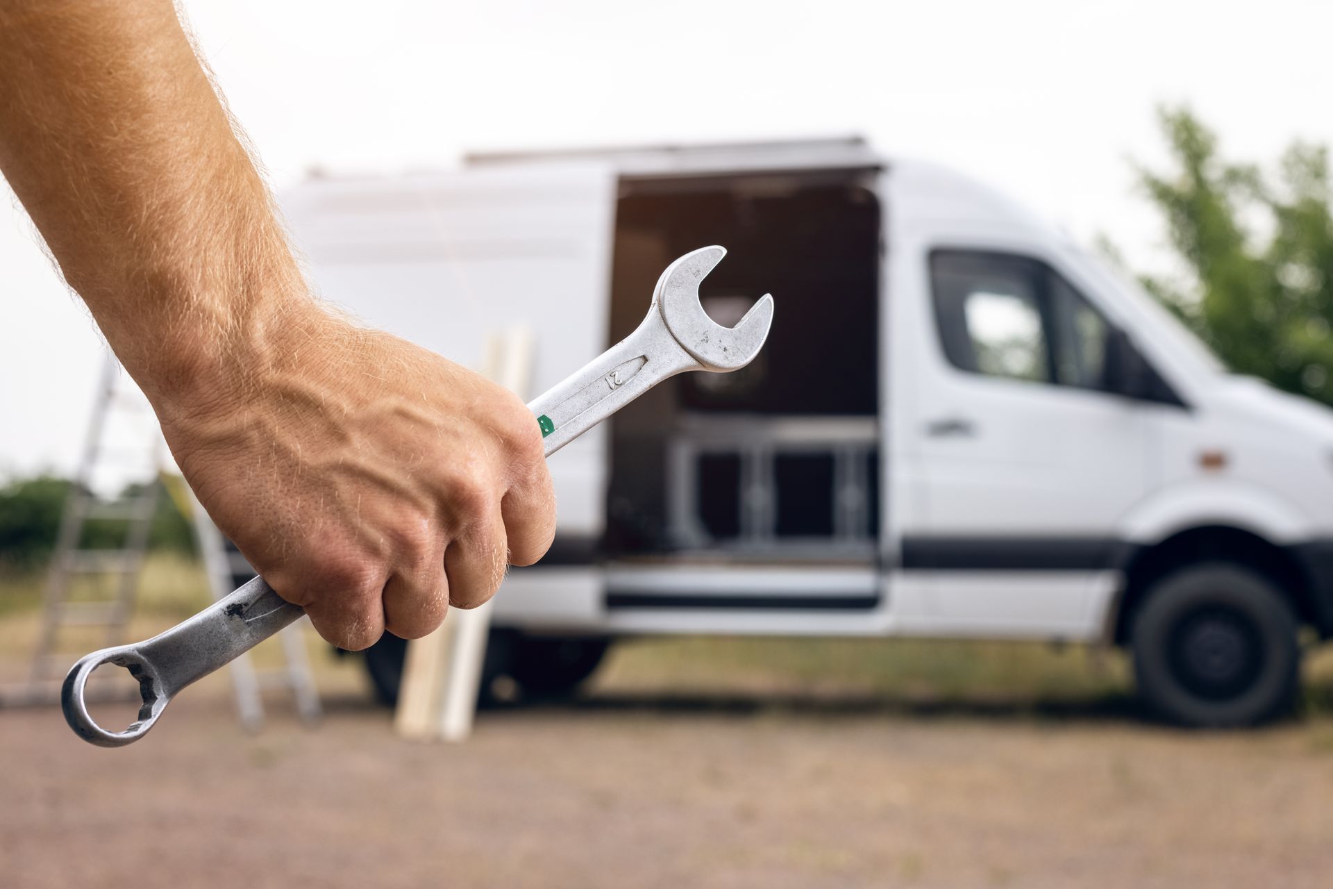 Hand holding a wrench in front of a white van with its side door open