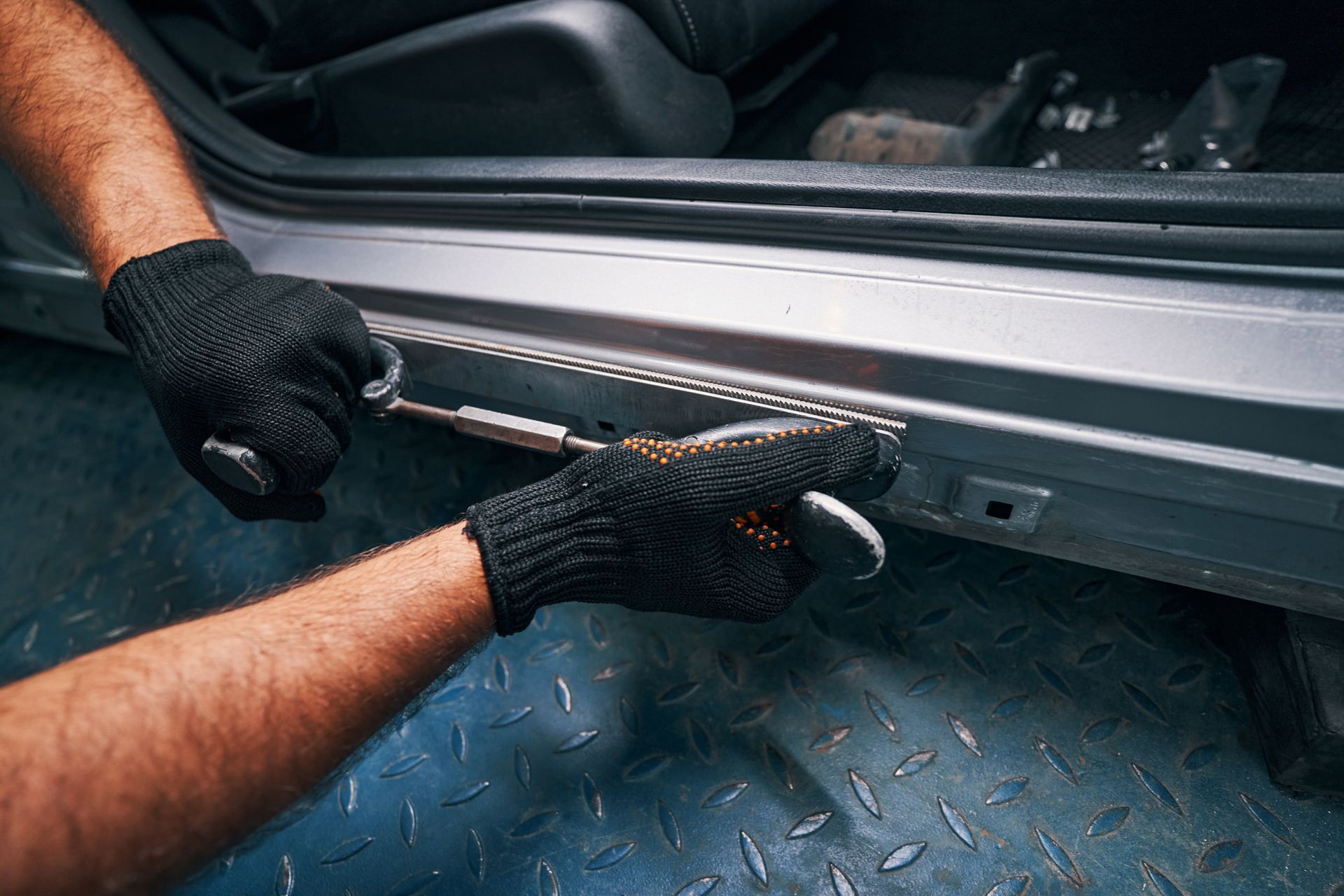 Gloved hands using a tool to install a black side step on a car threshold