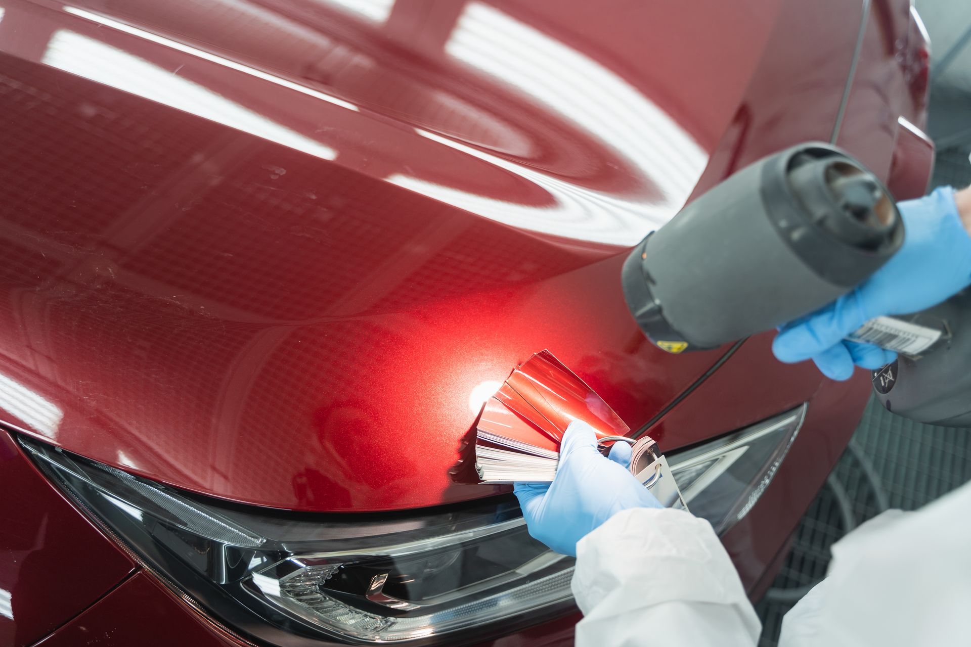 Technician spray-painting a red car hood with a spray gun in a workshop
