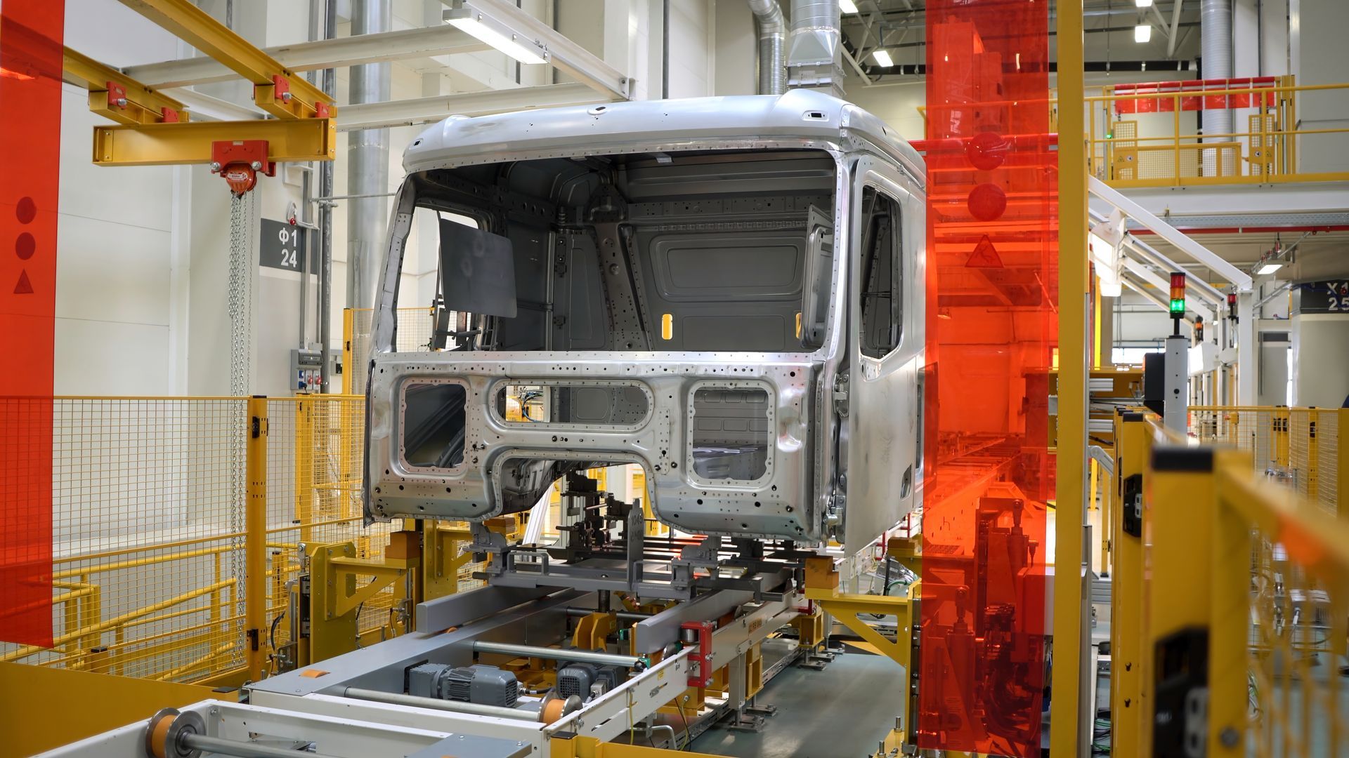 Silver vehicle body on an assembly line in a factory with orange machinery and safety rails