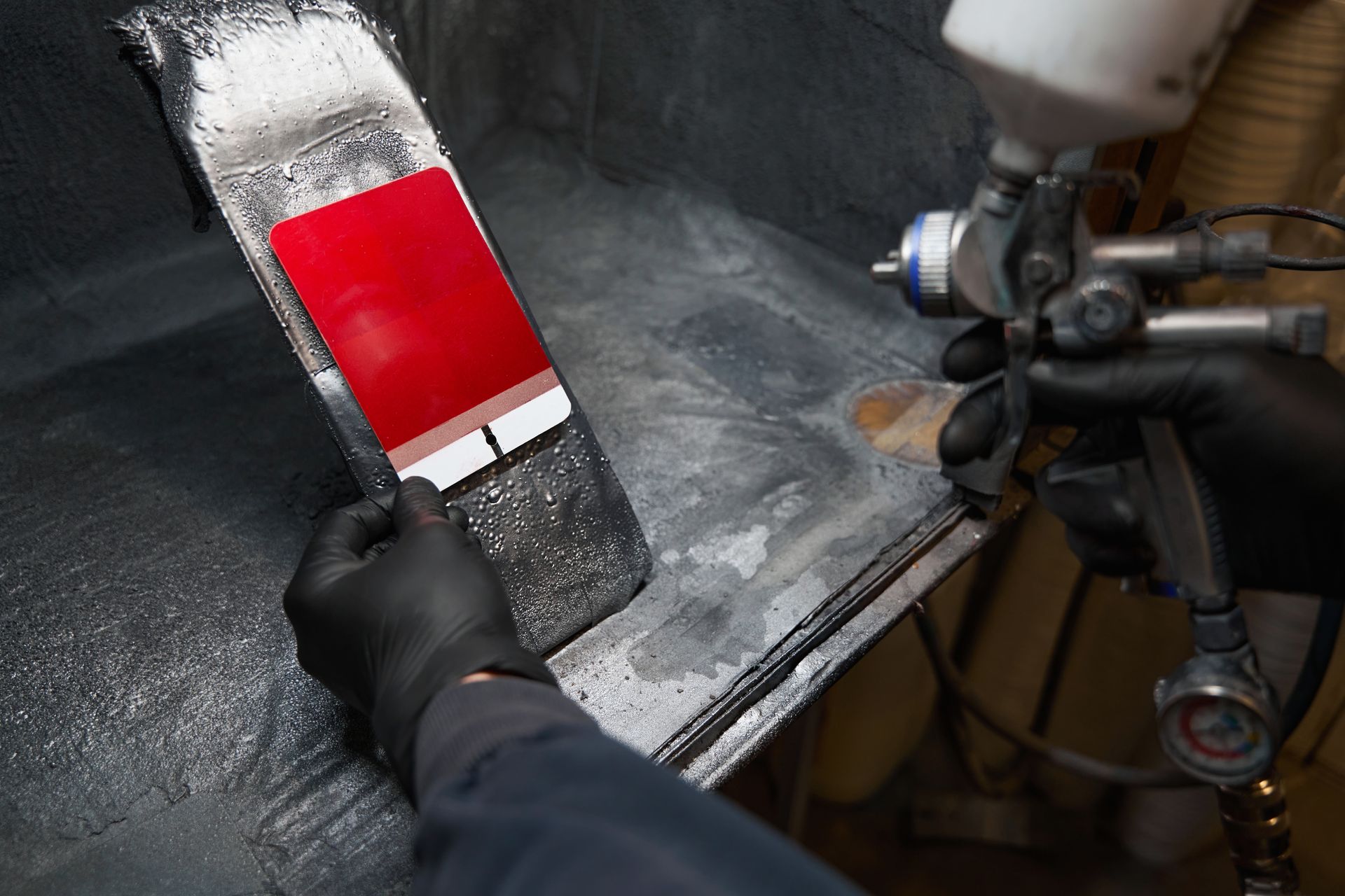 Gloved hand spray-painting a white and red board in a workshop booth