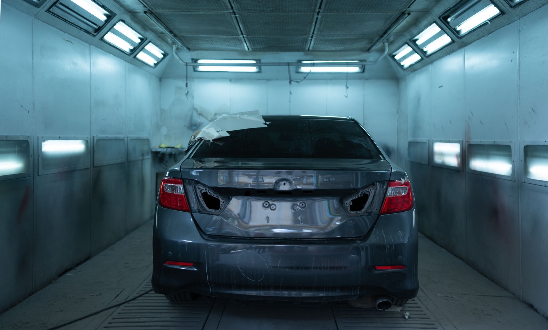 Dark gray sedan inside a blue-lit car wash bay, rear view.