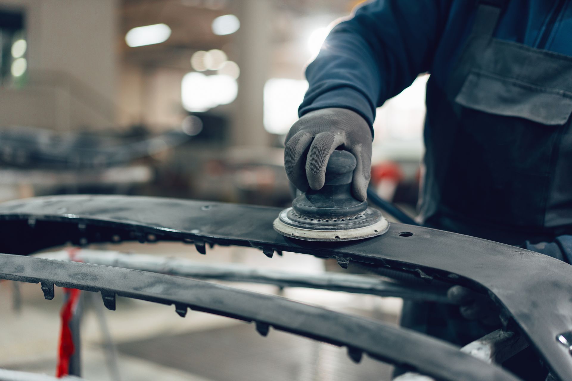 Gloved hand sanding a car panel in an auto body shop