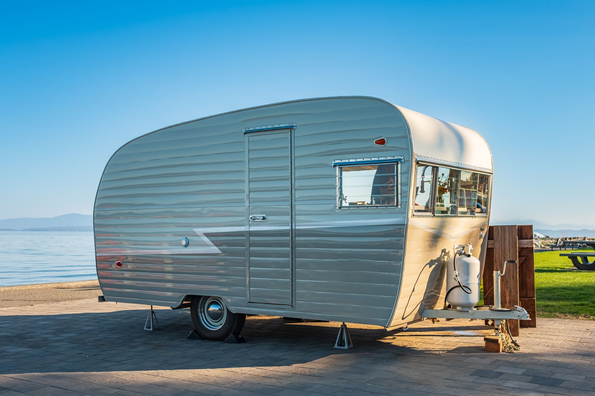 Silver camper trailer parked on a sandy beach by the sea under a clear blue sky