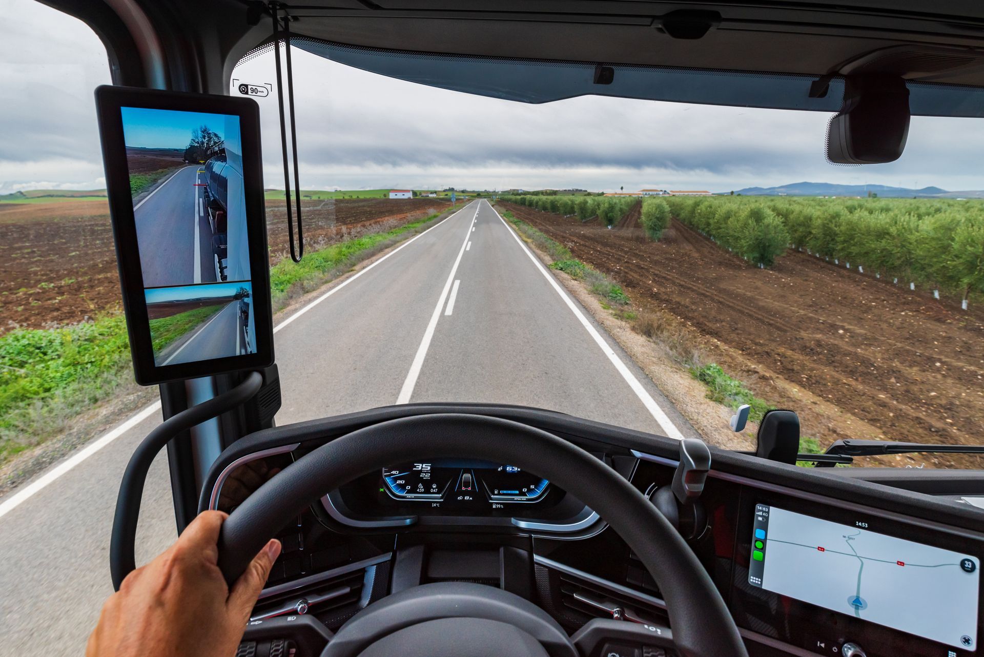 View from a truck cab driving down a straight rural road, with fields on both sides.