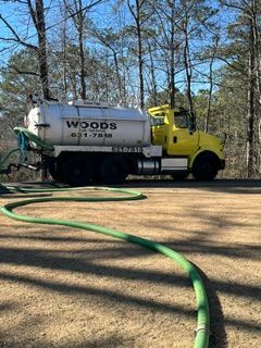 Yellow Woods tanker truck parked in a wooded yard with a green hose on the ground