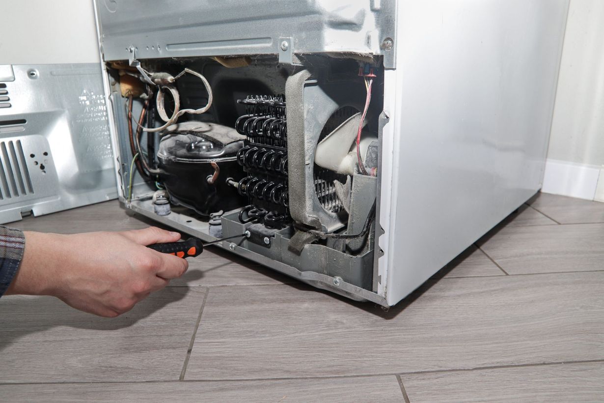 Person using a screwdriver to repair the open back of a dishwasher on a kitchen floor