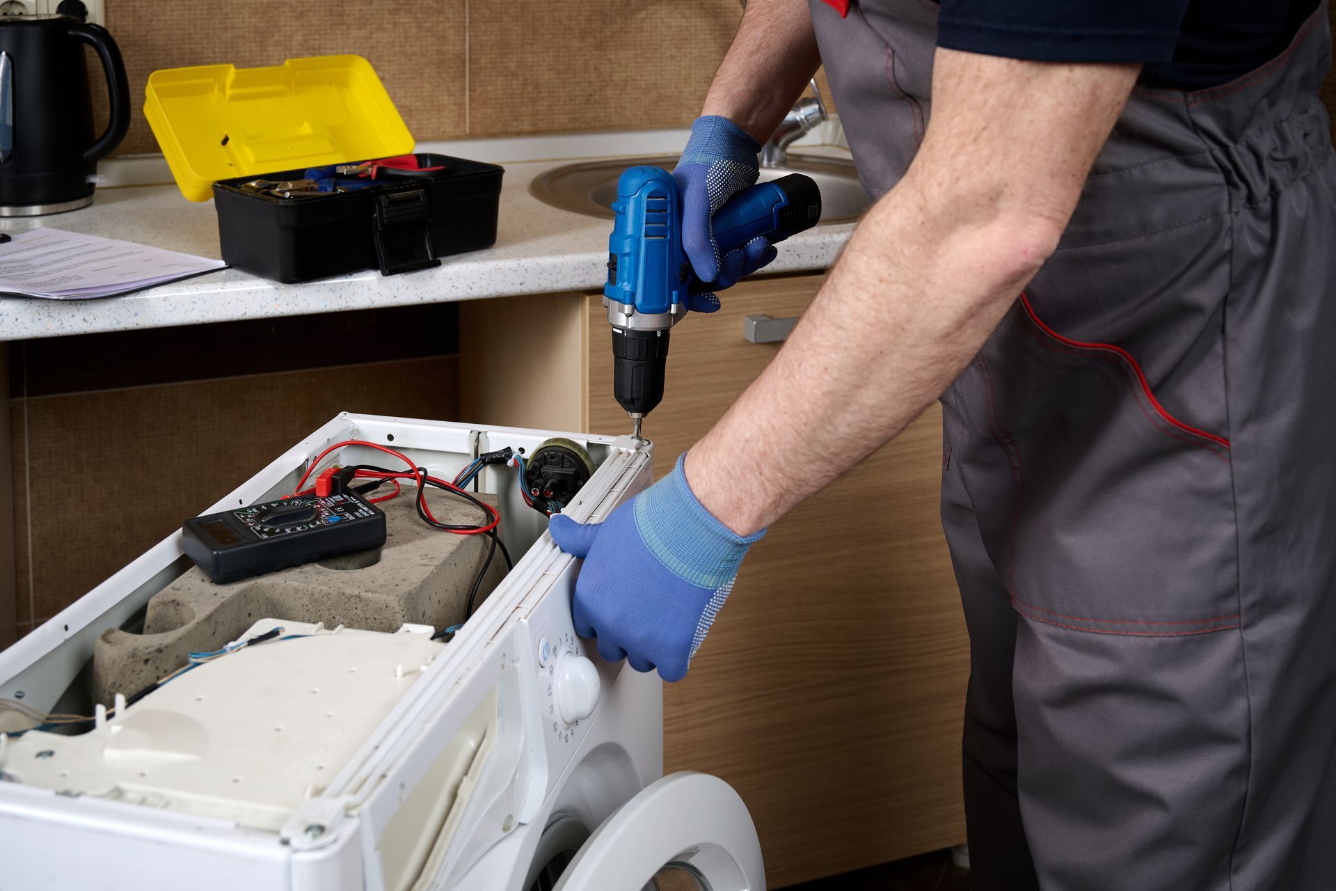 Technician using a blue drill to repair an appliance with its top panel removed